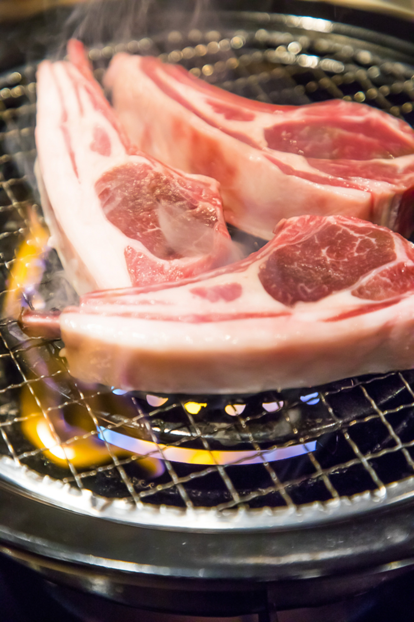 網の上で焼かれる骨付き肉と立ち上がる煙